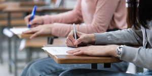 Students writing answers on an exam sheet in a classroom.