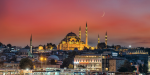 A breathtaking sunset view of Istanbul with illuminated mosques and a crescent moon in the sky.