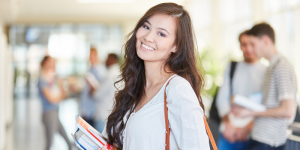 Smiling female student holding books, feeling confident about starting her Turkish language prep year.