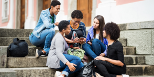 Group of international students sitting on steps and sharing content on a smartphone in Türkiye.